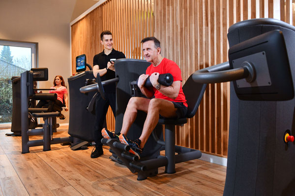 Mann trainiert an EGYM-Gerät unter Aufsicht eines Trainers in modernem Fitnessbereich