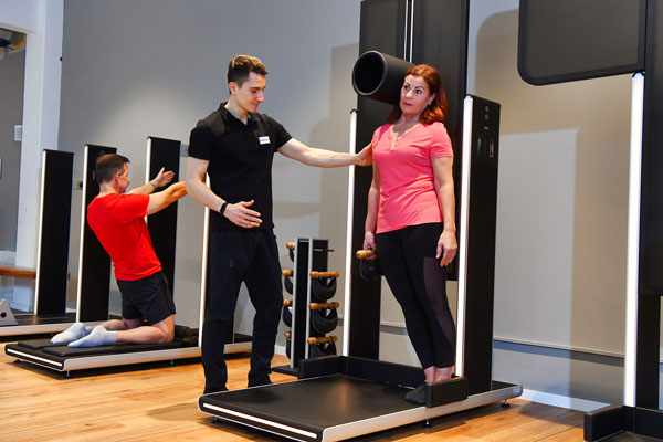 Trainer unterstützt Patientin bei Dehnübung an einem funktionellen Trainingsgerät